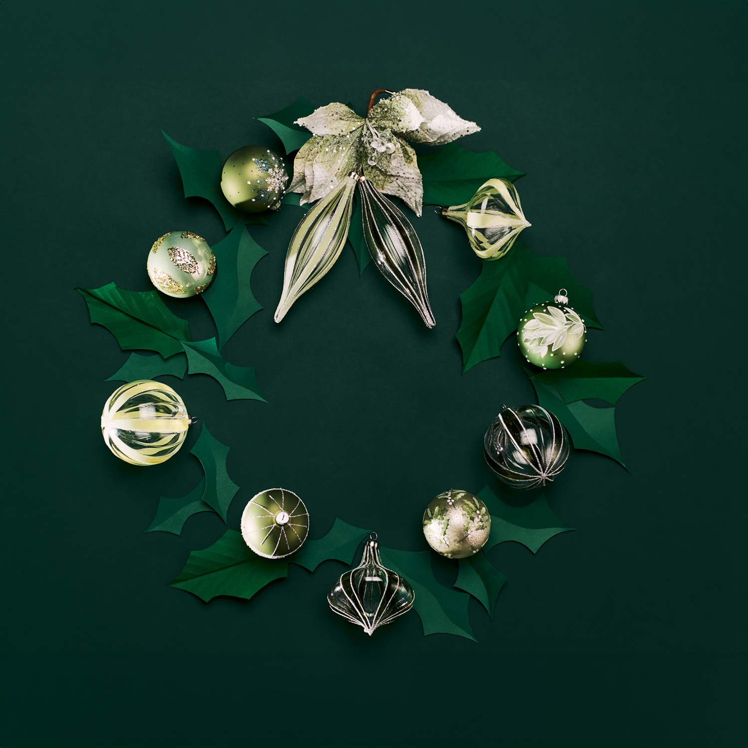 Festive wreath with green ornaments and leaves on a dark green background.