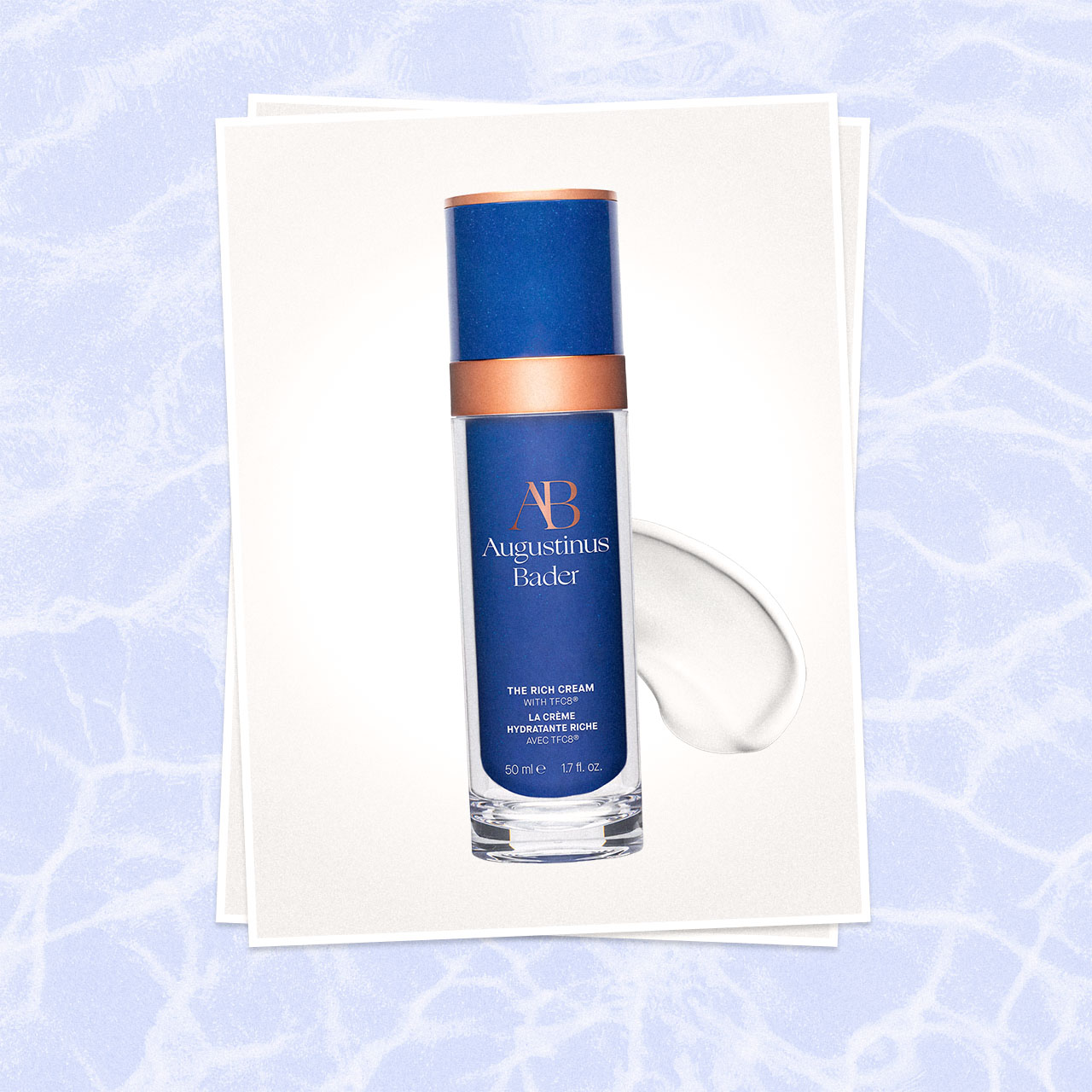 Blue bottle of Augustinus Bader Rich Cream skincare product with copper band, displayed on cream card with water droplet swipe
