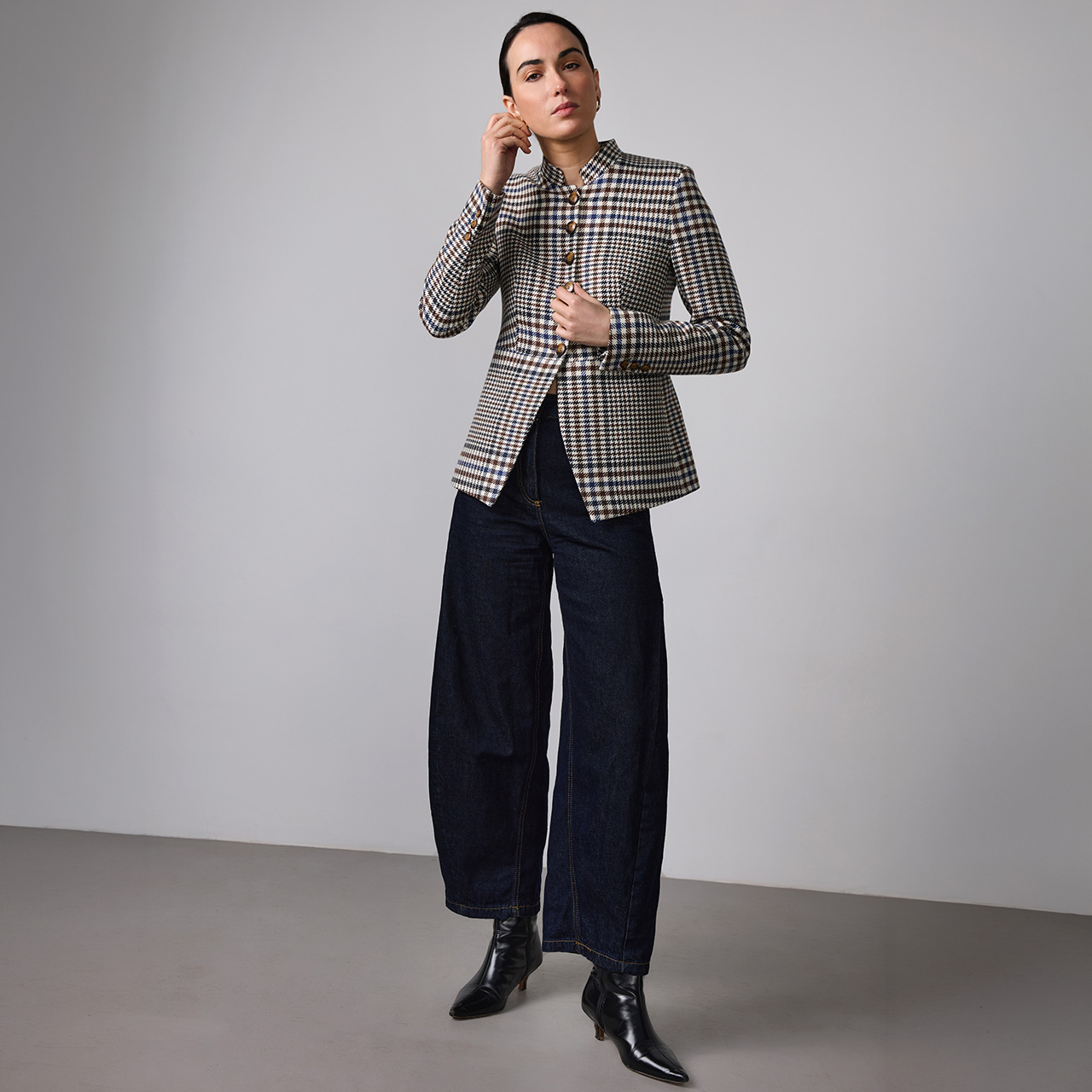 Person in a checked blazer, dark wide-leg pants, and black boots poses against a plain background.
