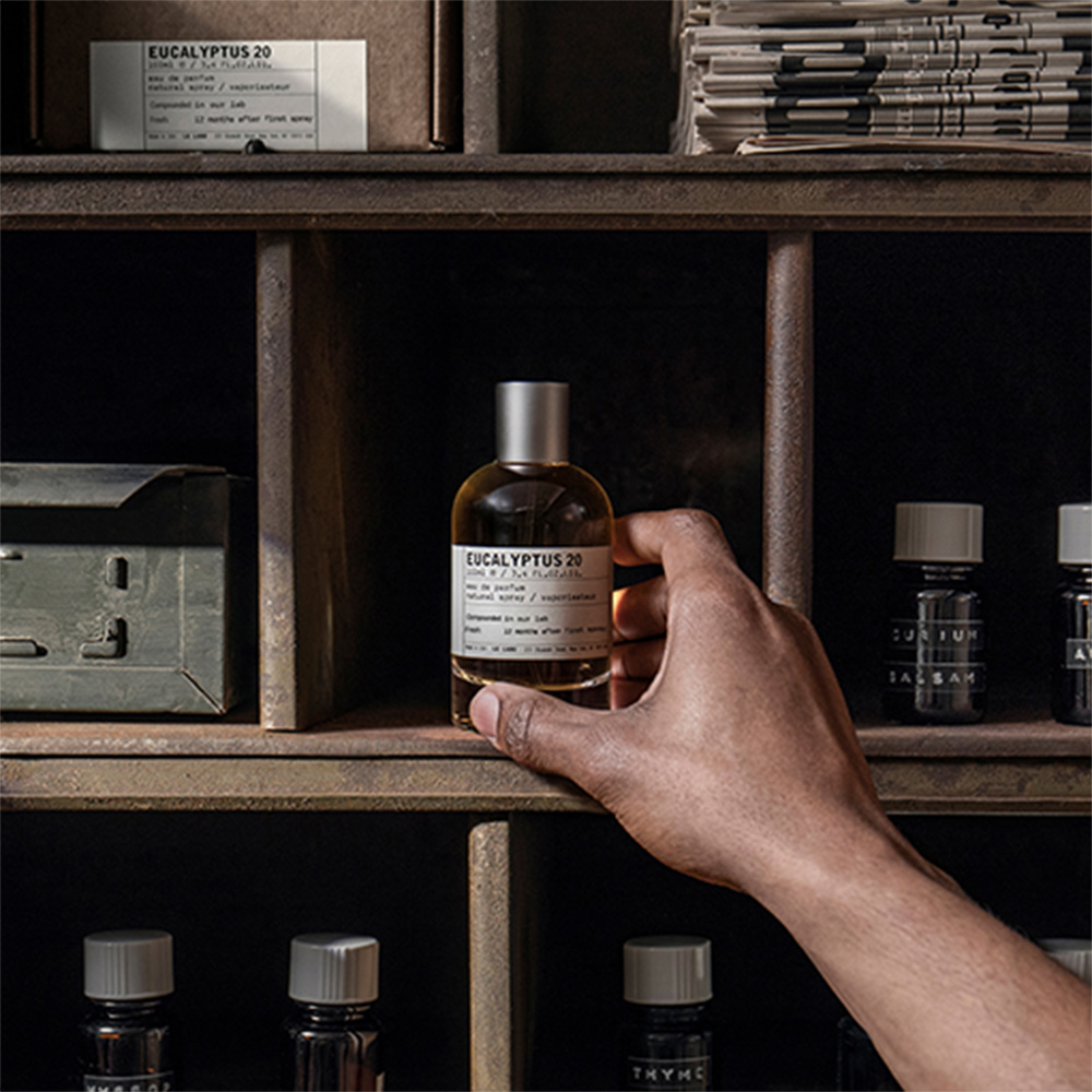 Hand holding Eucalyptus 20 fragrance bottle from shelf unit displaying multiple scent bottles and storage boxes