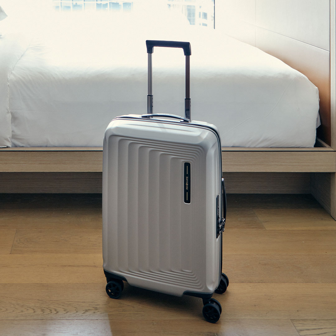 Silver suitcase with a retractable handle on a wooden floor next to a bed.