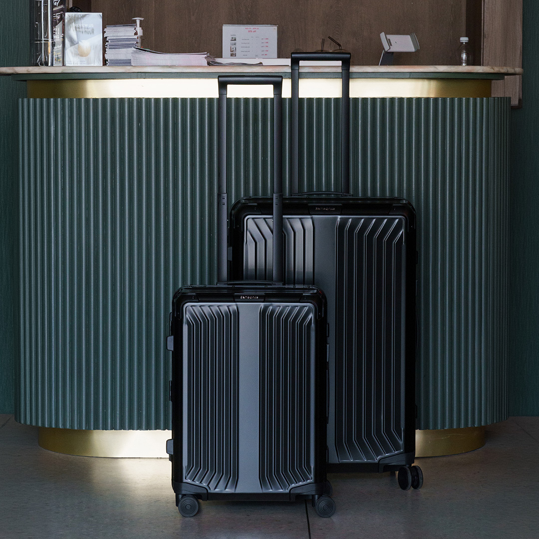 Two black hard-shell checked suitcases with ribbed design and retractable handles displayed at a curved green reception desk