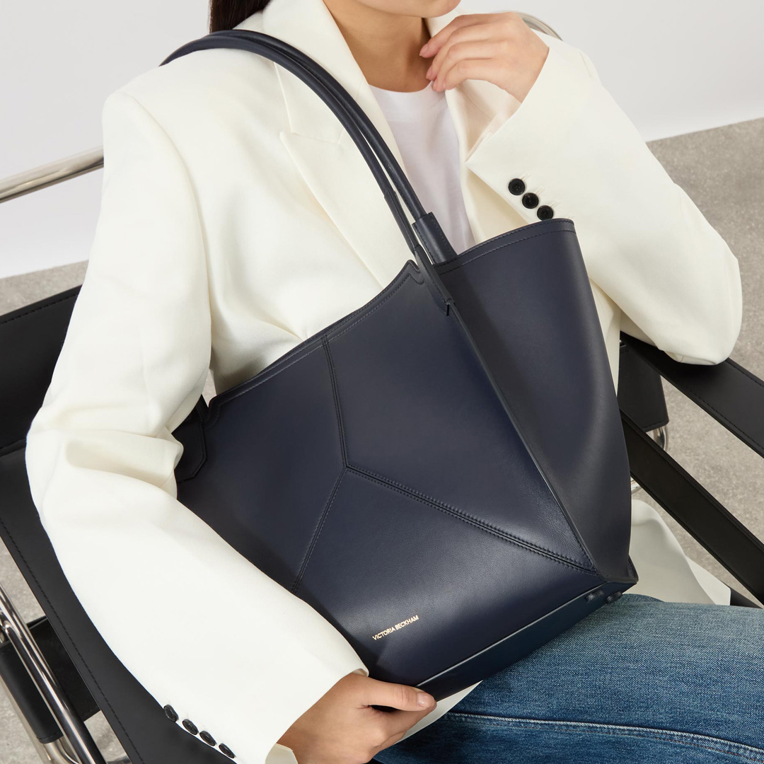 Woman wearing cream blazer holding navy leather tote bag with dual handles