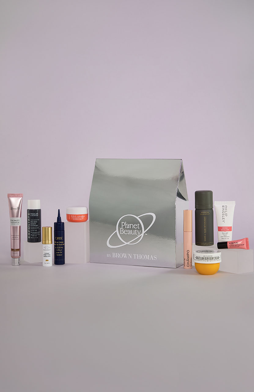 Various skincare and beauty products arranged around a metallic 'Planet Beauty' bag on a light purple background.