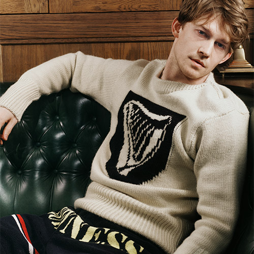 Person lounging on a green leather couch, wearing a cream sweater with a black harp design.
