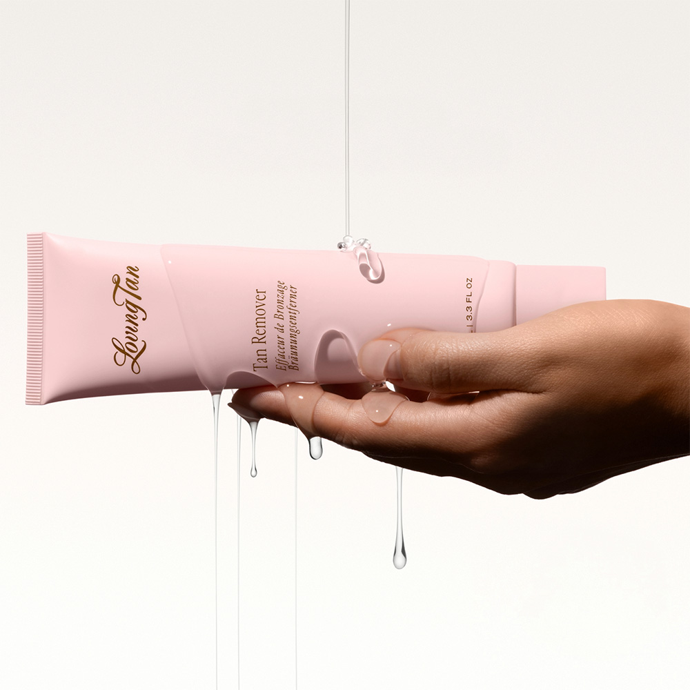 Hand holding Loving Tan pink exfoliating tan remover tube with product dripping