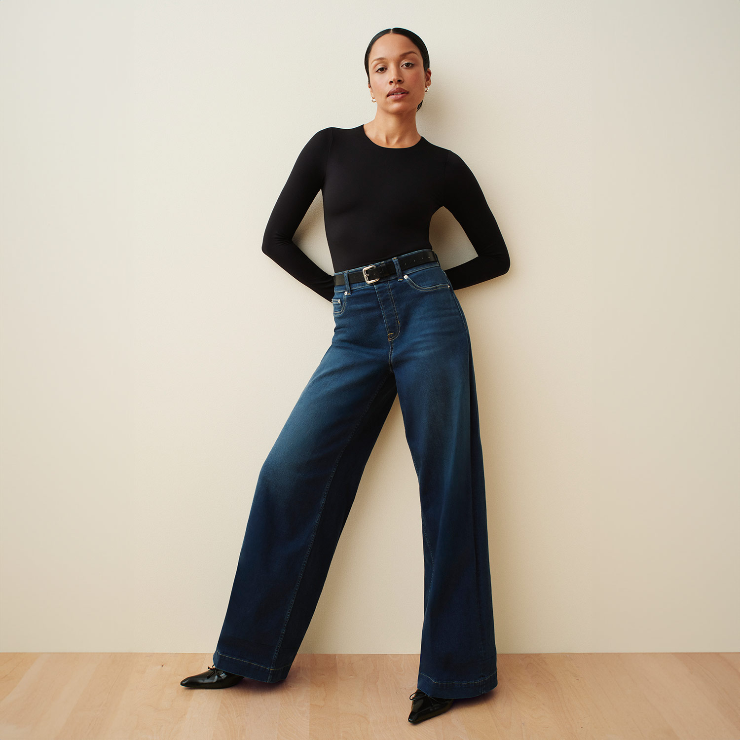 Woman wearing a black top and wide-leg jeans, with a minimalist style.