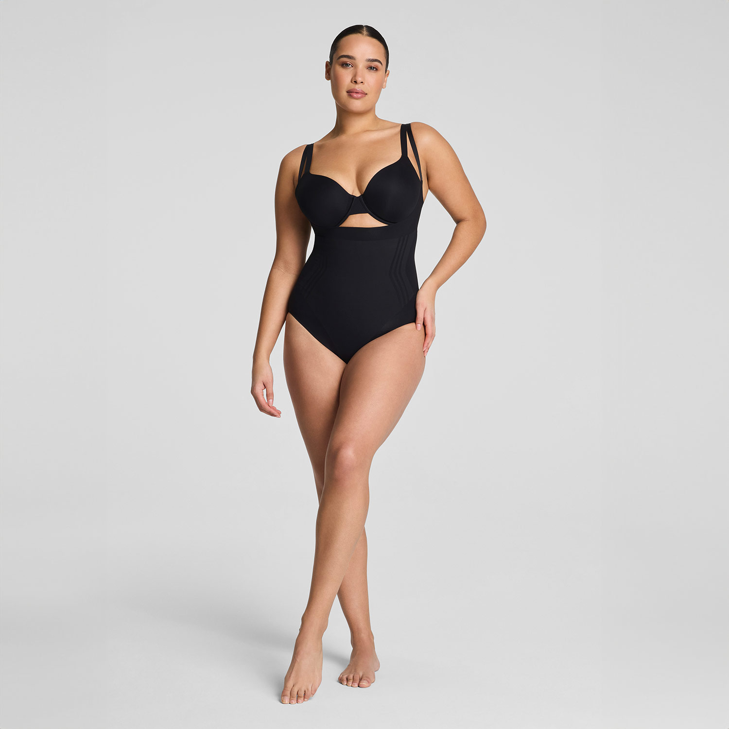 A woman poses in a black one-piece swimsuit against a neutral background.