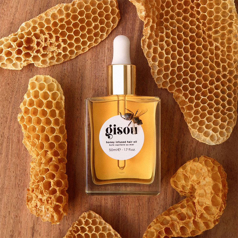 Gisou honey-infused hair oil bottle surrounded by honeycomb pieces on wooden surface