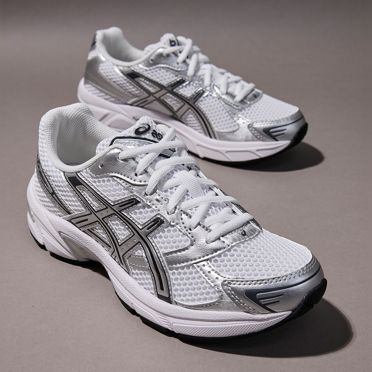 Two white and silver trainers with black accents on neutral background
