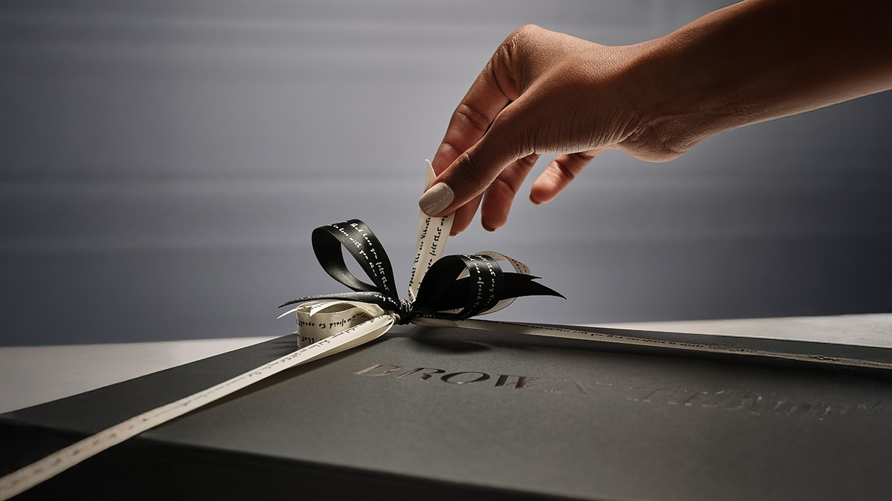 A hand tying a black ribbon on a gift box.