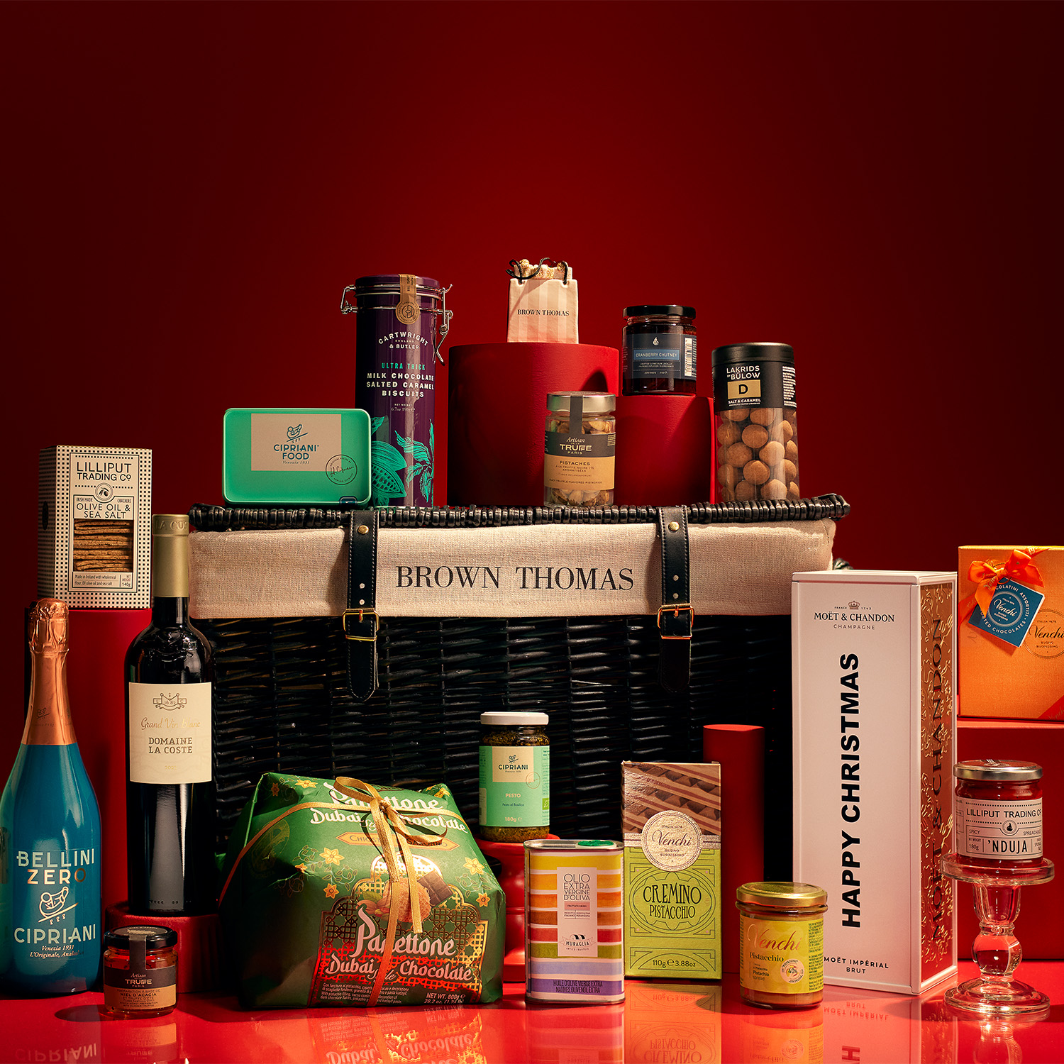 A variety of gourmet food and drink items are displayed against a red background, centered around a basket with 'Brown Thomas' on it.