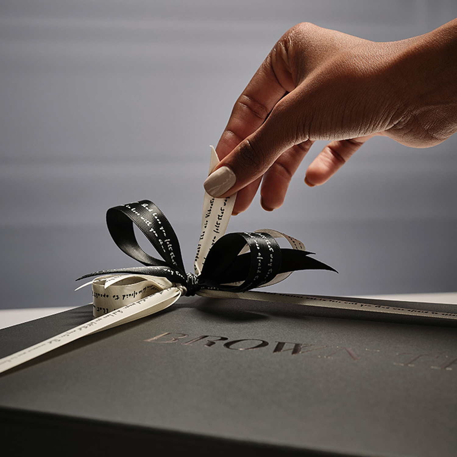 A hand gently adjusts the black ribbon bow on a sleek, dark gift box.