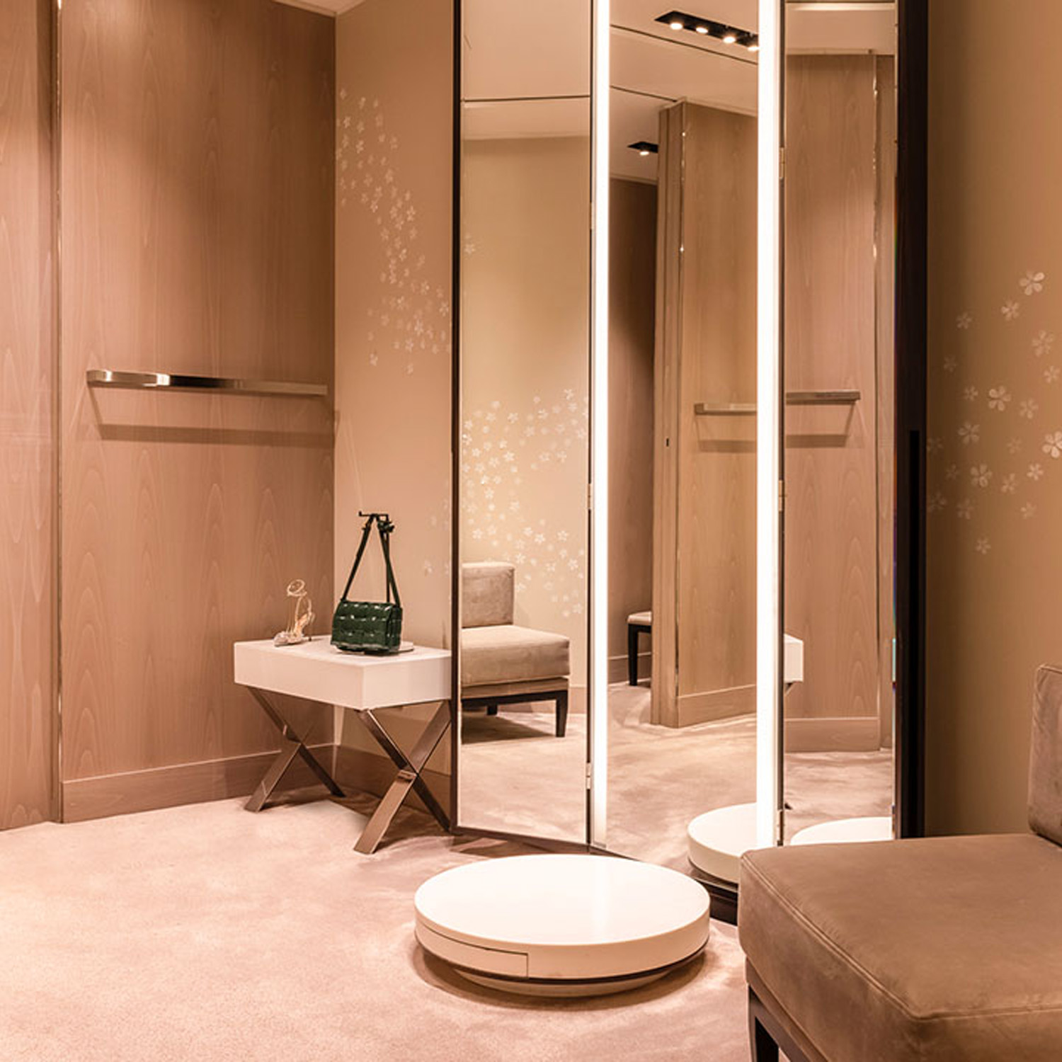 A stylish dressing room with beige walls, a large mirror, seating, and a side table.
