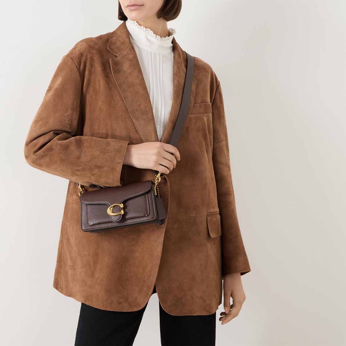 Person in a brown suede jacket with a white blouse underneath, holding a small brown handbag.