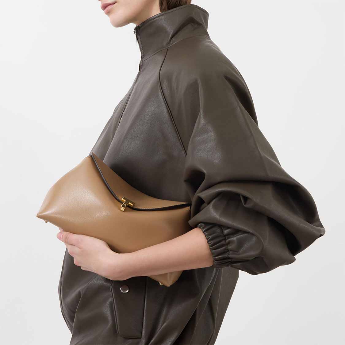 Person in a brown jacket holding a tan leather clutch.