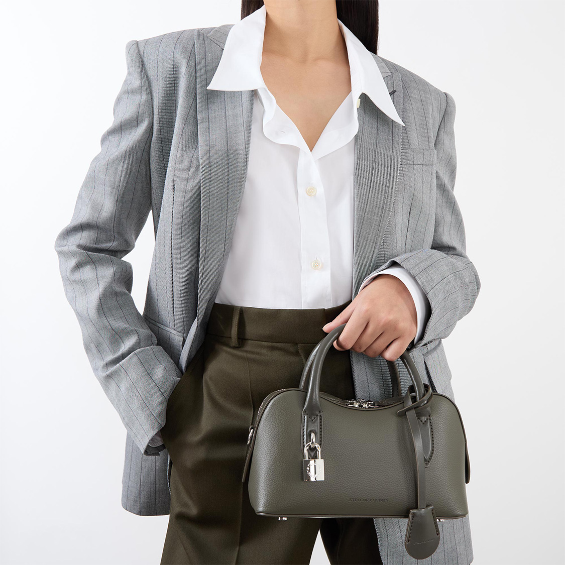 Person in a gray suit and white shirt holding a stylish green handbag.
