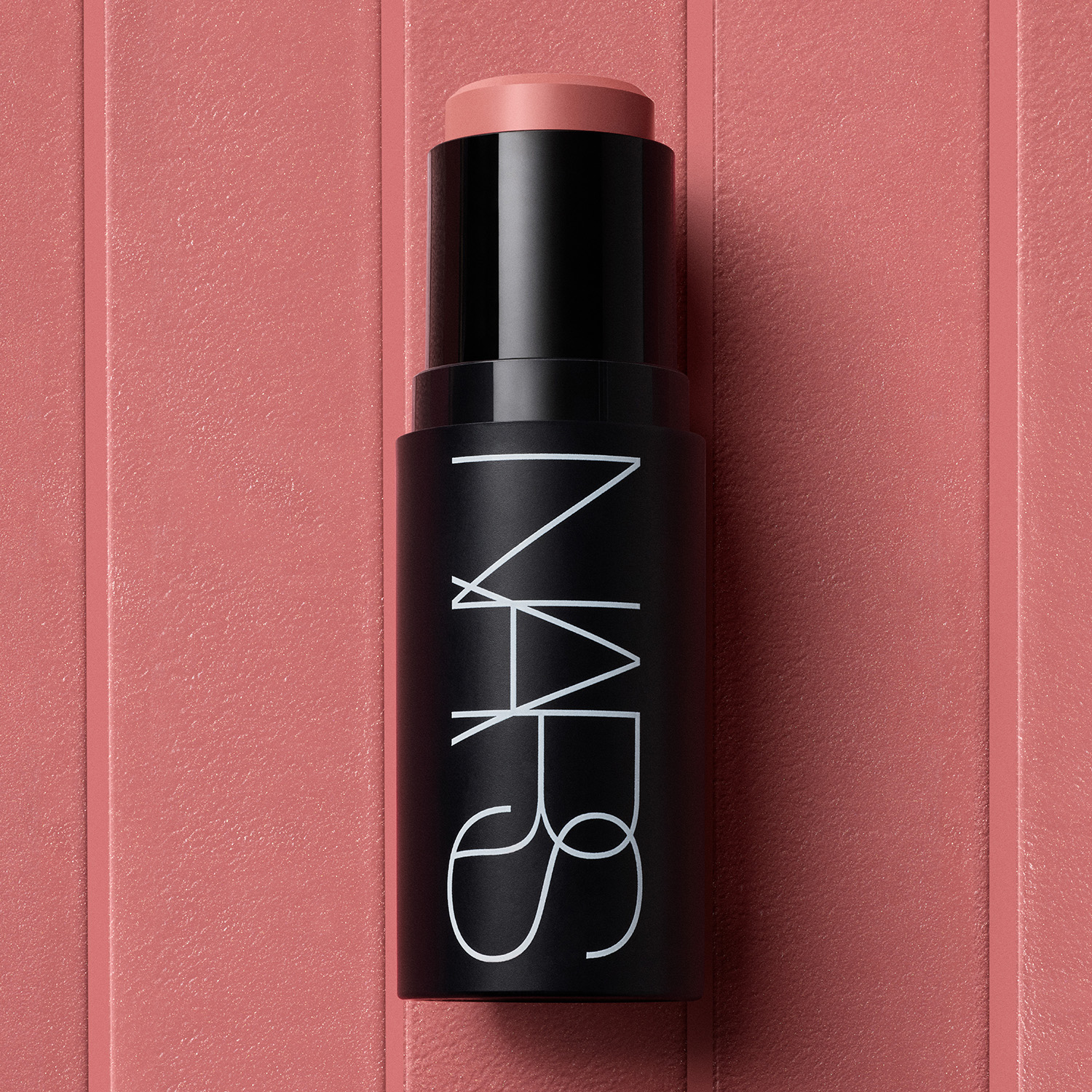 A NARS makeup stick with a black casing and pinkish shade, set on a matching textured background.