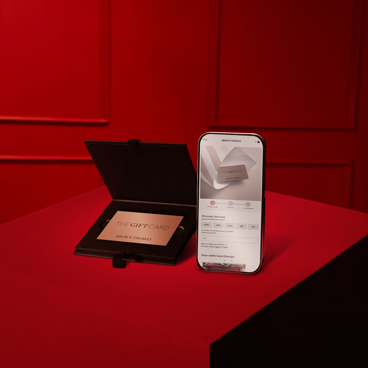 A smartphone and a gift card display in a black case on a red surface.