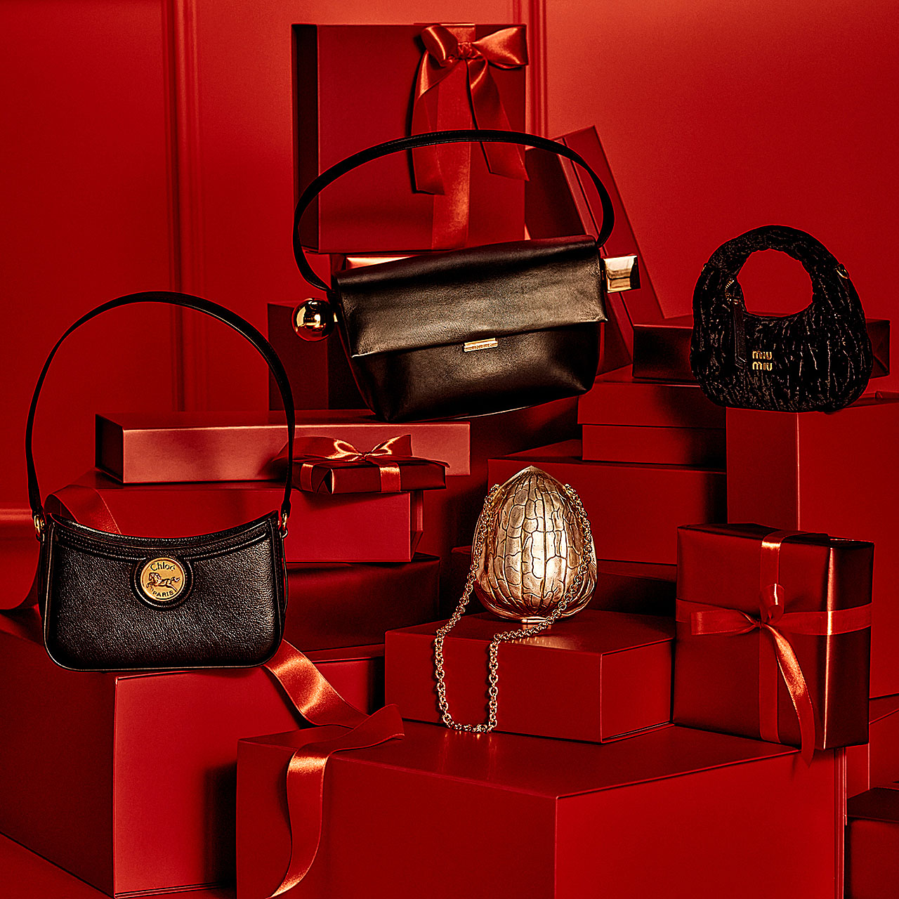 Luxury handbags displayed on stacked red gift boxes with ribbons.