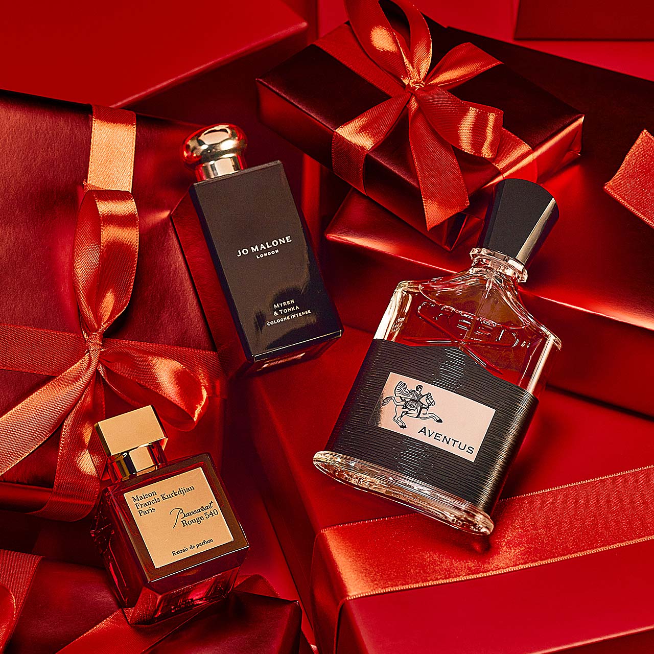 Three perfume bottles surrounded by red gift boxes tied with ribbons.