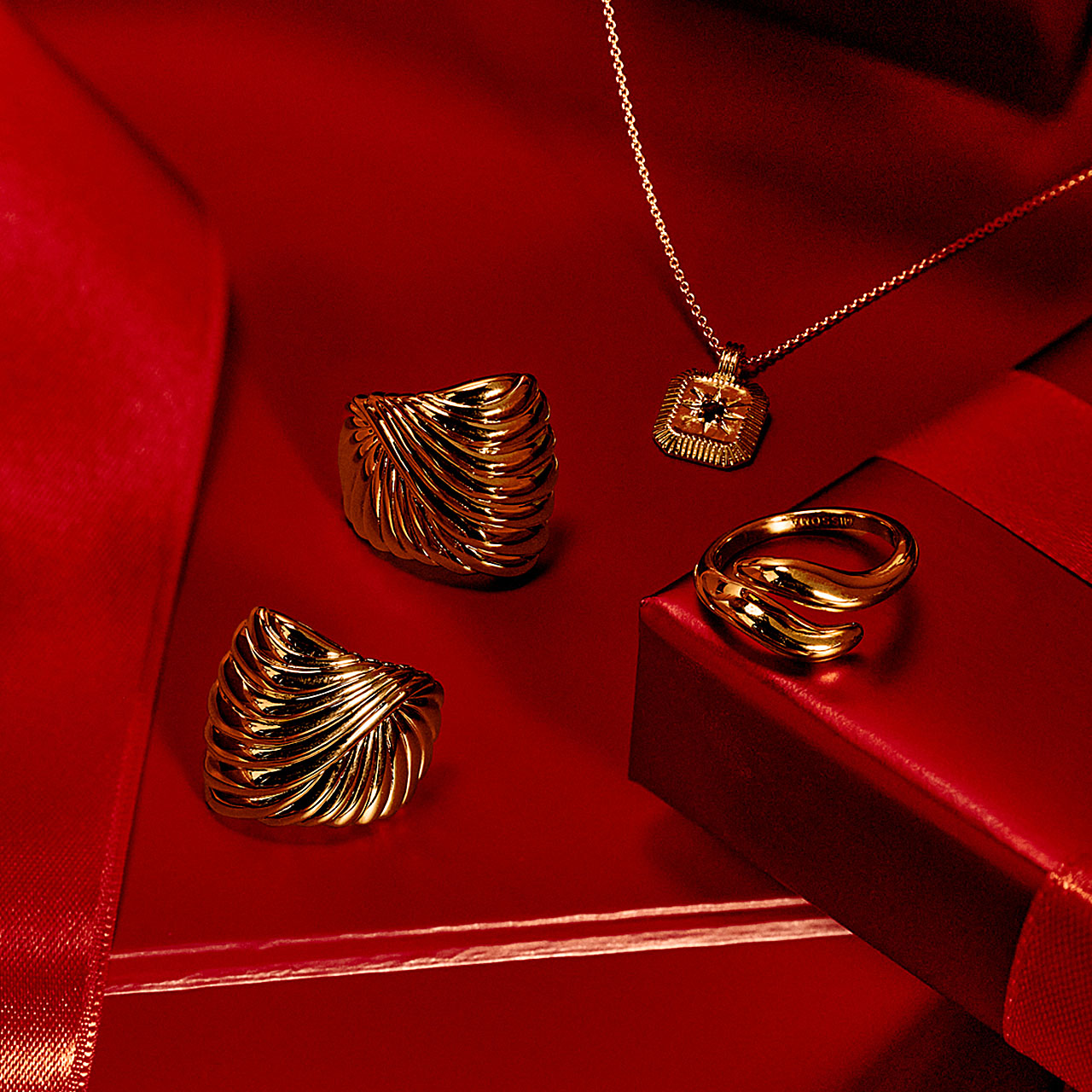 Gold jewelry displayed on a red surface, including rings and a necklace, with a luxurious presentation.