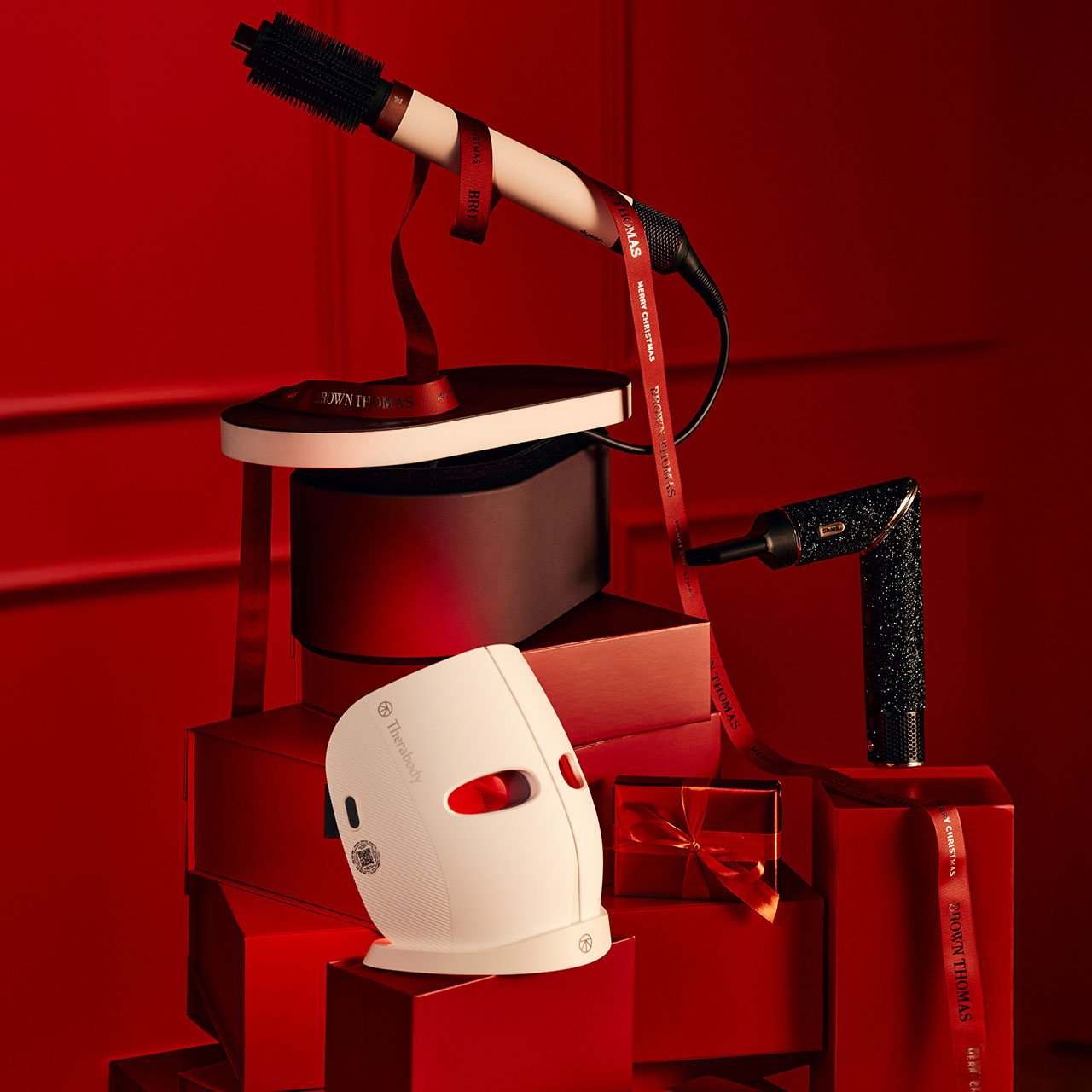 A collection of hair styling tools elegantly arranged on red gift boxes, with ribbons and a warm red background.