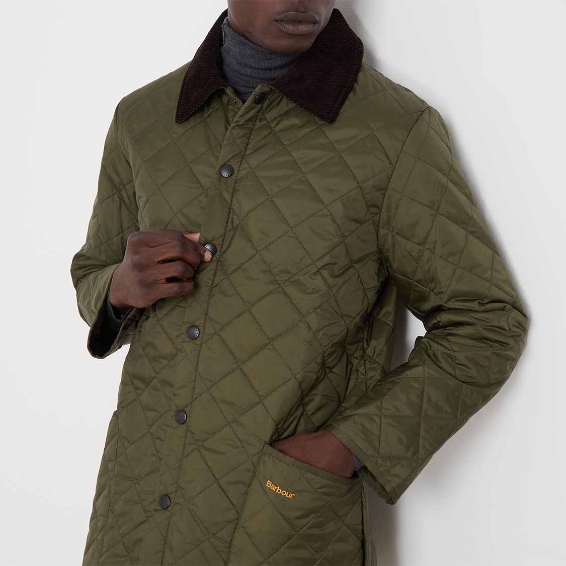 Person wearing a quilted olive green coat with a dark collar against a light background.