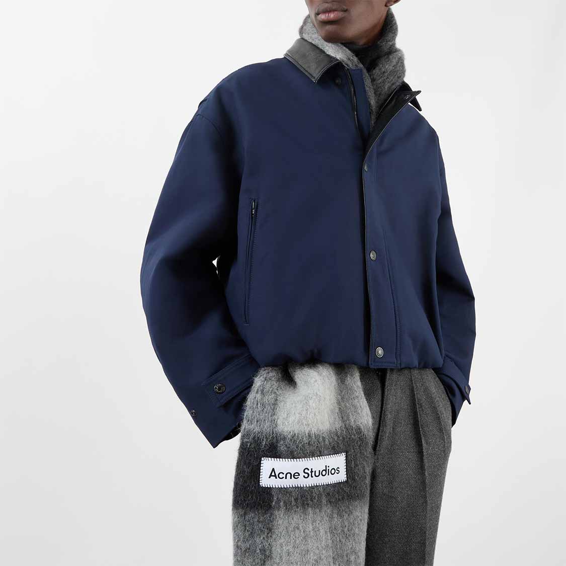 Person wearing a blue jacket, gray scarf, and gray pants, with an Acne Studios label visible on the scarf.