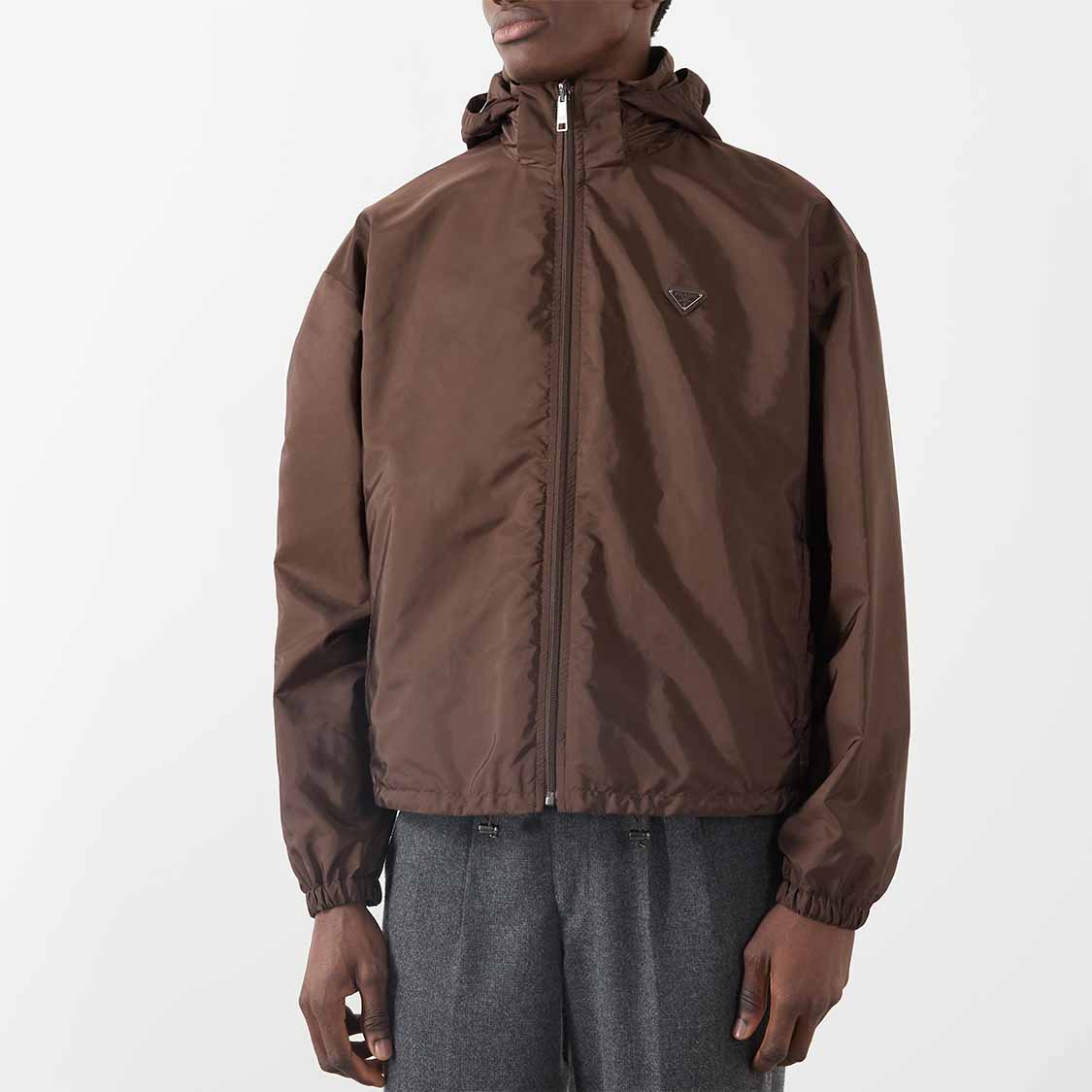 Person wearing a brown hooded jacket and gray pants against a light background.