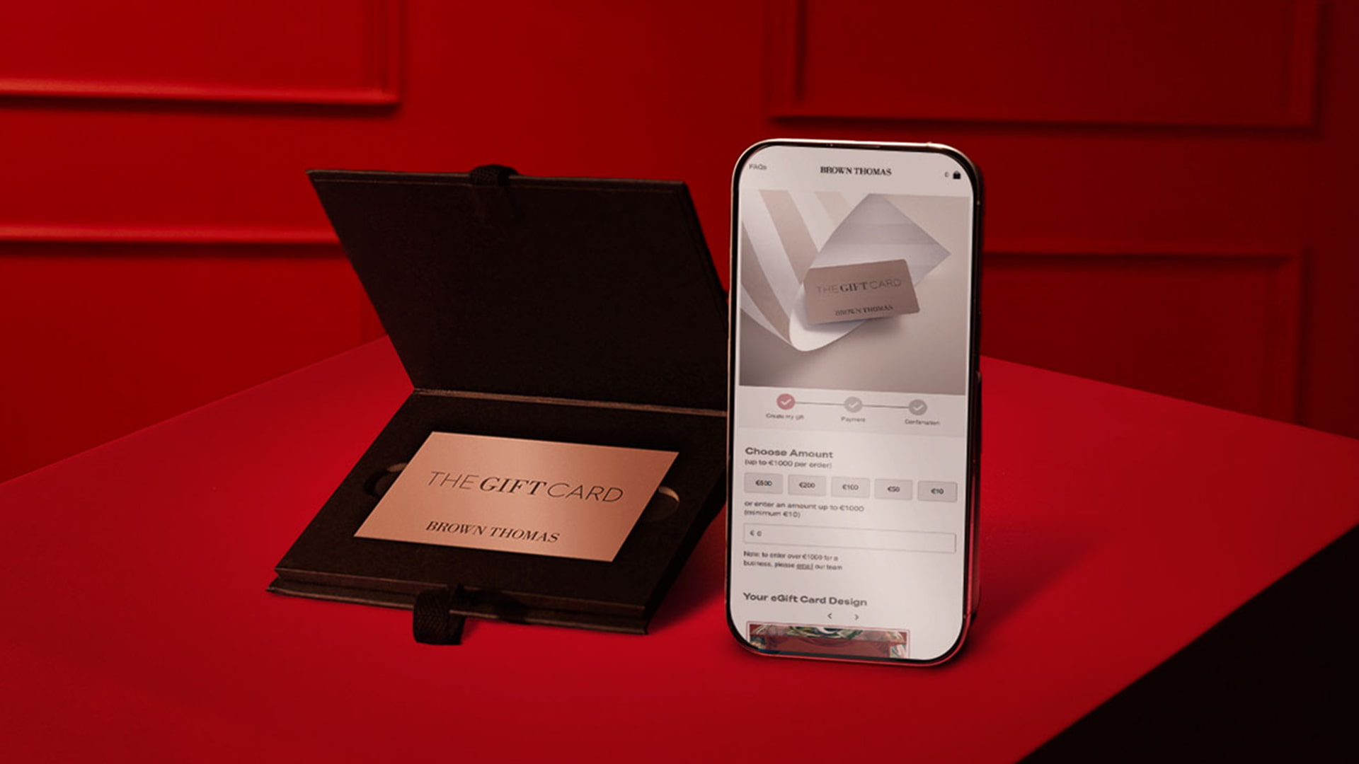 A gift card and a smartphone displaying a product image are placed on a red table.