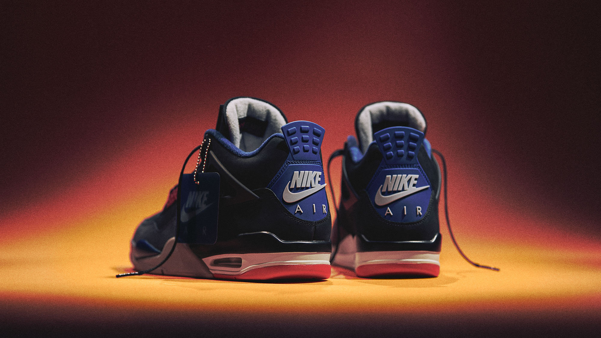 A pair of blue Nike Air sneakers is lit dramatically against a dark background.
