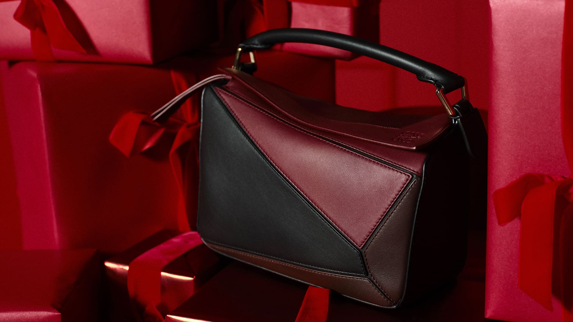 A stylish handbag with geometric patterns is displayed on red gift boxes with matching red ribbons.