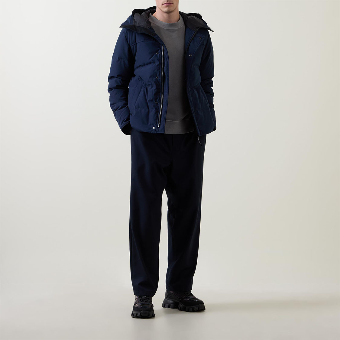 Person in a blue puffer jacket over a gray shirt, with dark pants and black shoes, standing against a light background.