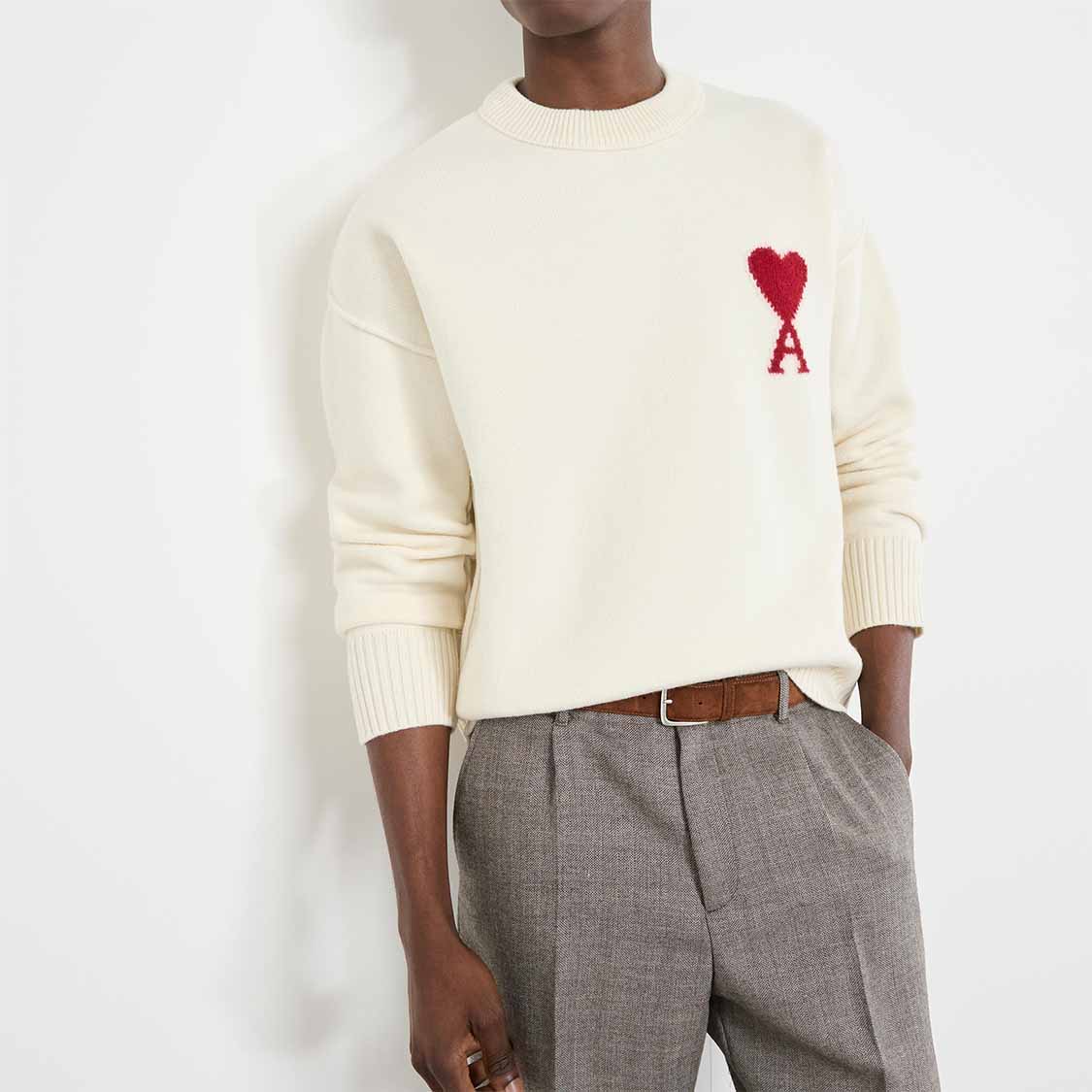 Person wearing a white sweater with a red heart and the letter 'A,' paired with gray pants.