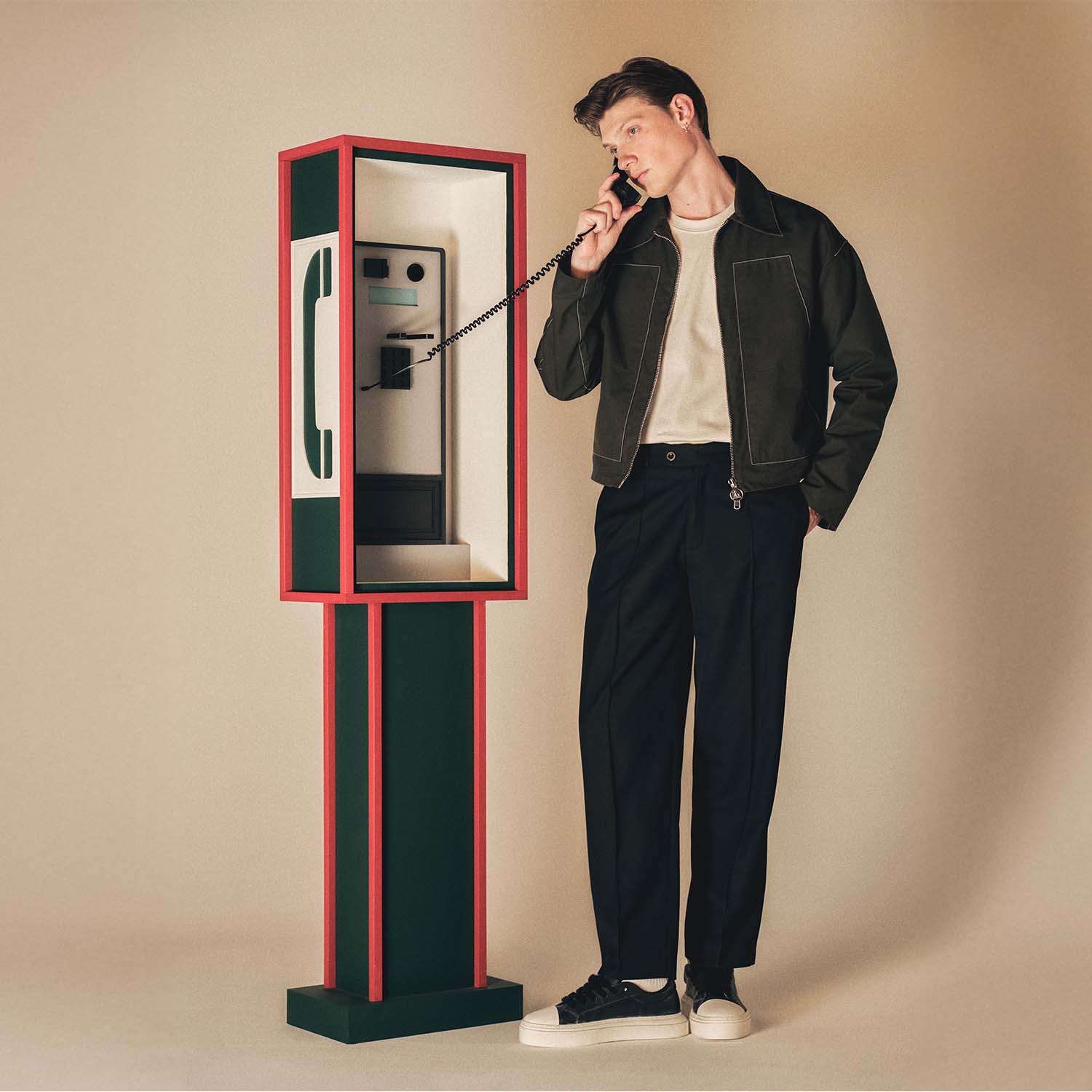 A person in casual attire uses a retro-style phone booth, standing against a neutral background.