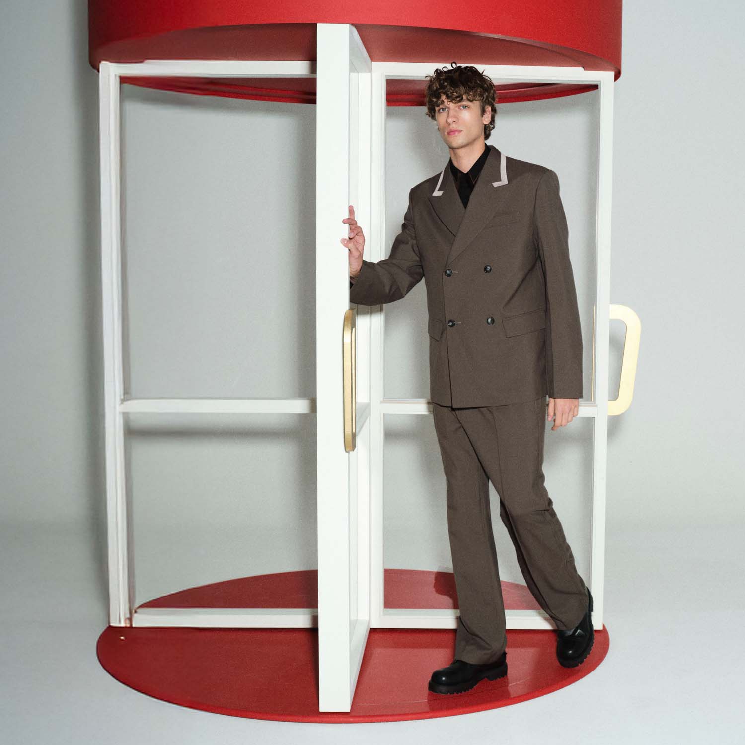 A person in a brown suit steps out of a red and white revolving door.
