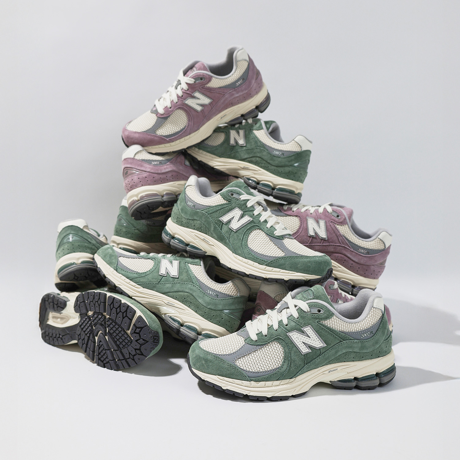A pile of New Balance sneakers in green and purple hues on a plain background.