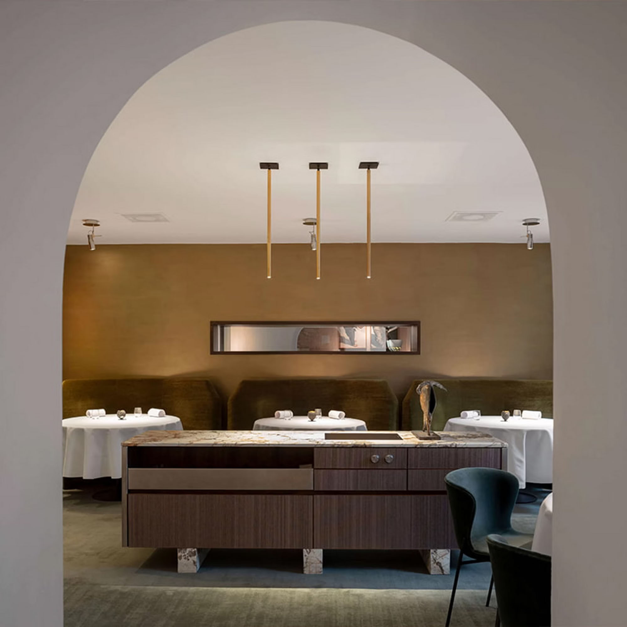 Elegant dining room with arch entry, modern lighting, set tables, and a central wooden cabinet.