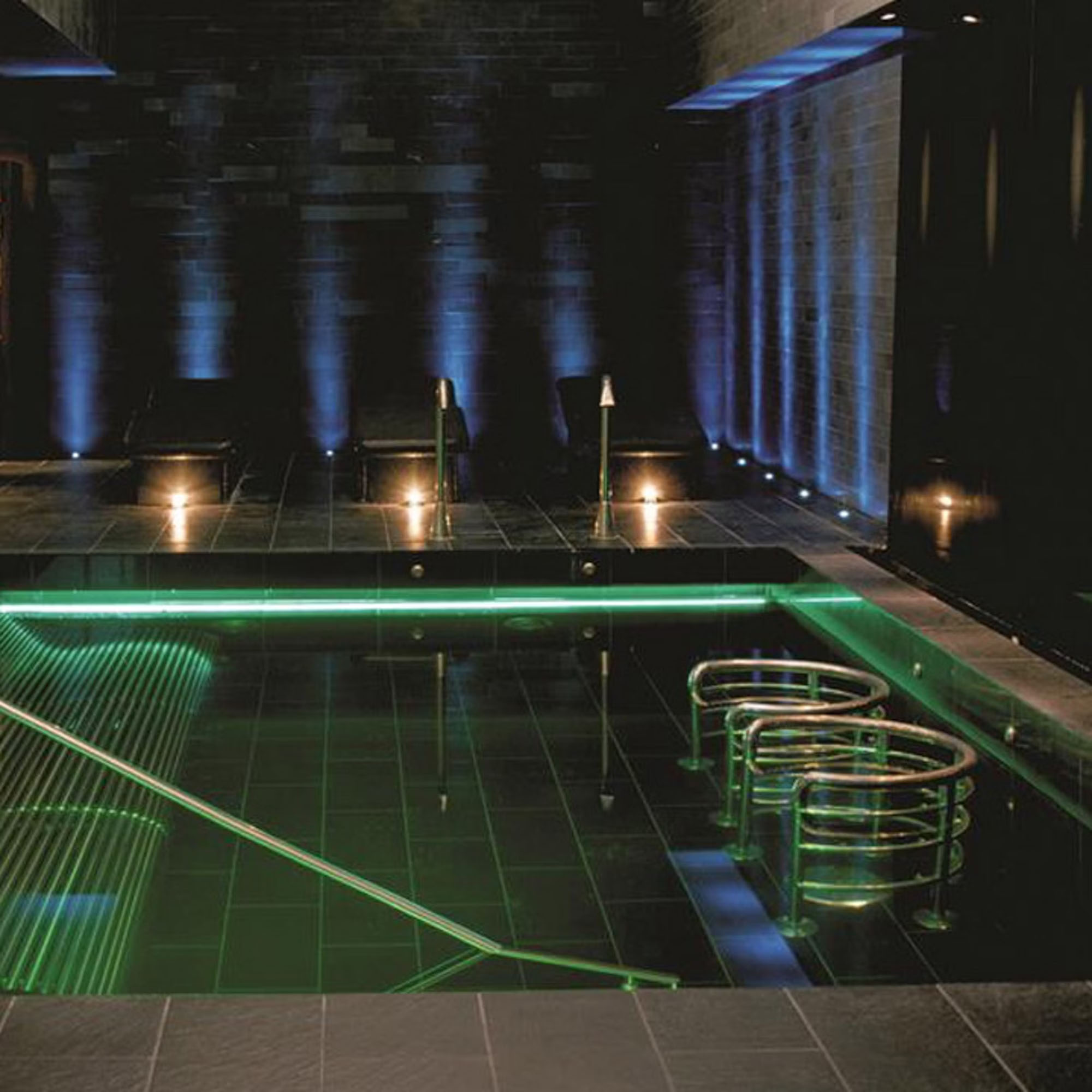 Elegant indoor pool area with ambient lighting, featuring blue and green hues.