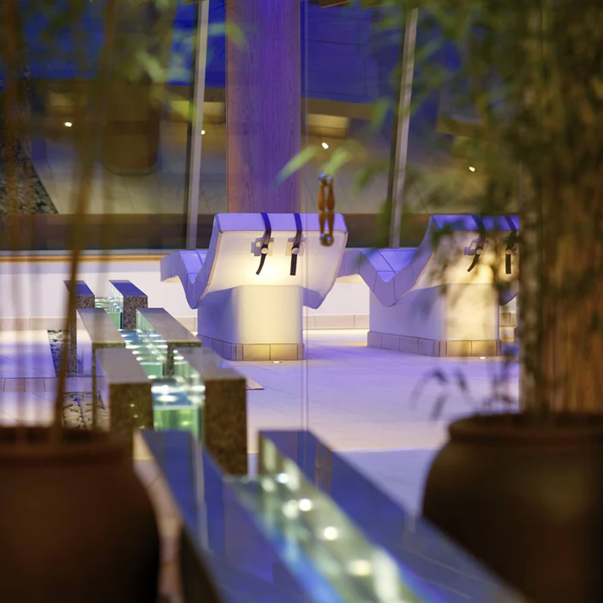 A modern lounge area with sleek white chairs, glass tables, and potted plants, illuminated by soft blue lighting.