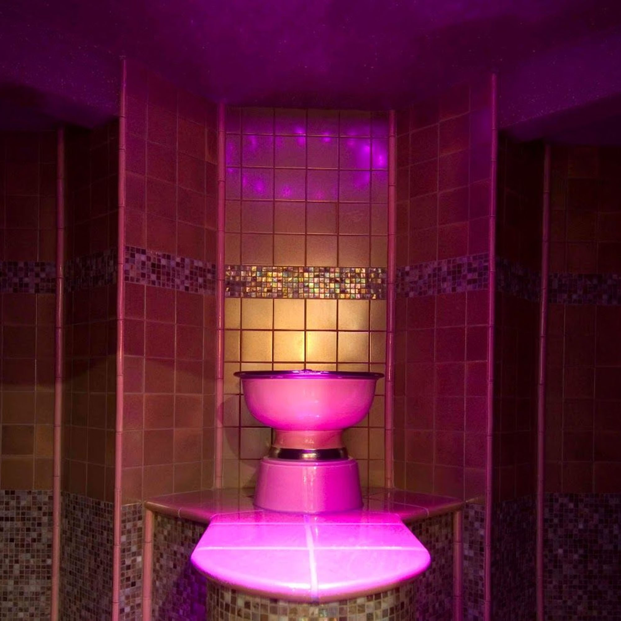 A dimly lit room with mosaic tiles and a central glowing pink pedestal or fountain.