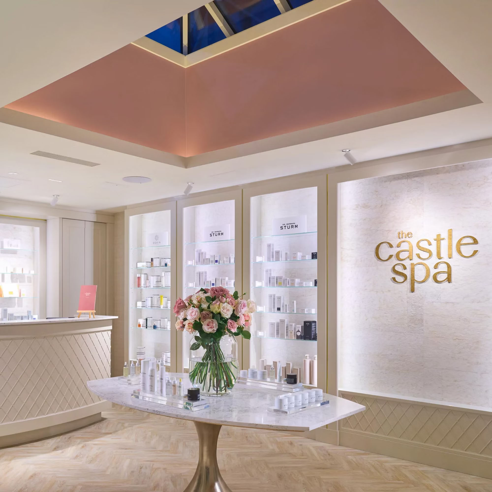 Bright spa interior with a marble table displaying products, floral arrangement, and 'the castle spa' sign on the wall.
