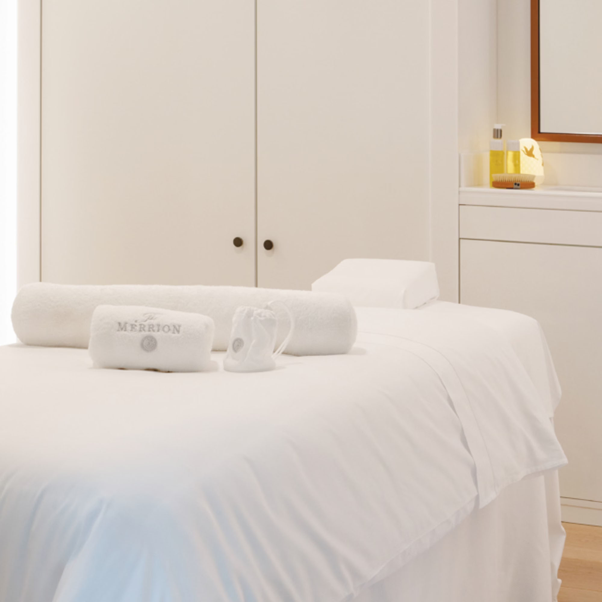 A serene spa room with a massage table, rolled towels, and a small shelf with candles and oils.