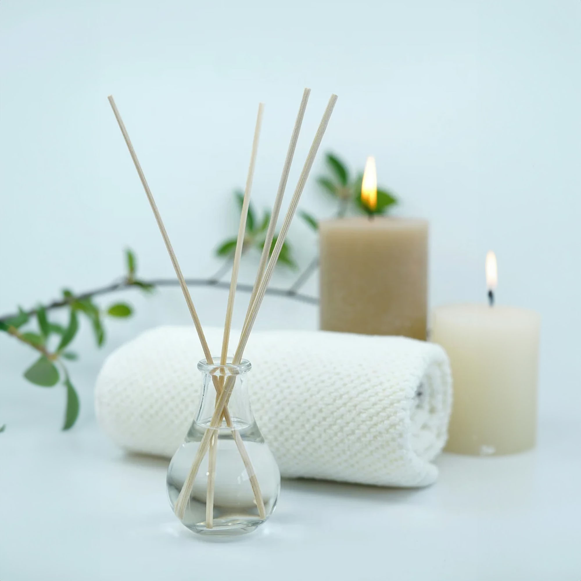 Aromatic diffuser, rolled towel, candles, and green branch create a serene spa-like setting.