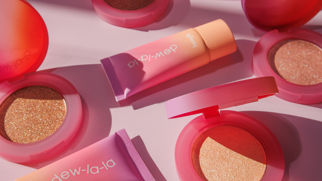 Cosmetics display featuring Benefit blushes and creams in pink packaging, arranged under soft lighting.