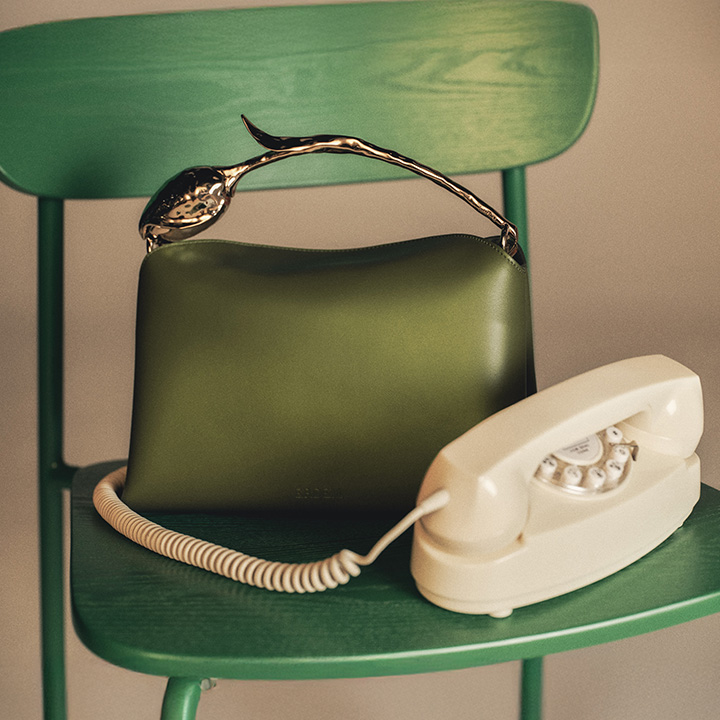 A green chair holds an olive green handbag with a metal handle and a vintage white rotary telephone.
