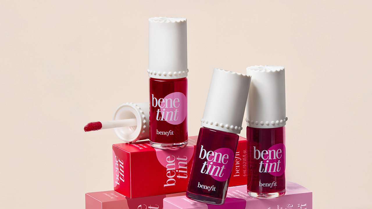 Three bottles of Benetint lip and cheek stain are displayed with red packaging and an open applicator wand.