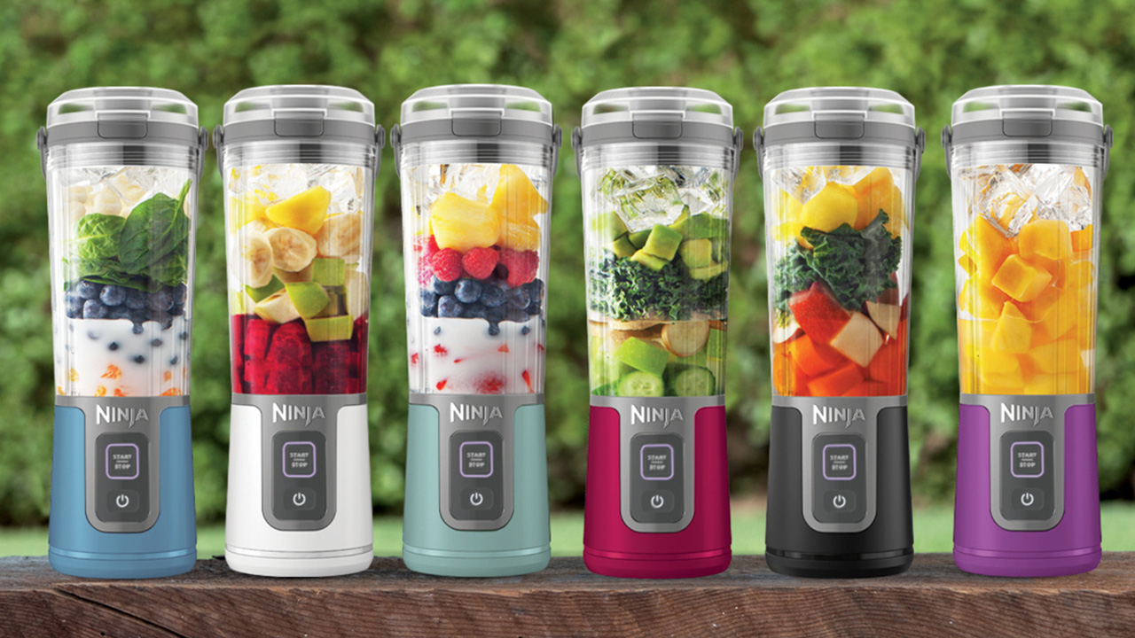 Six Ninja blenders are filled with various fruits and vegetables, each with different colored bases, set outdoors.