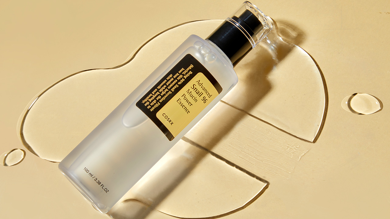 A skincare bottle lies on a beige surface with liquid droplets around it.